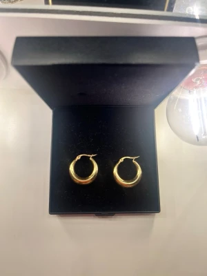 Guldpläterade creoler örhängen - Säljer ett par klassiska creoler i guldpläterad metall. Örhängena har en rund, tjock form och stängs med enkel klicklås. Perfekta för dig som gillar stilrena och tidlösa accessoarer. Levereras i svart ask.