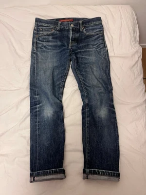 Slim fit selvedge archive jeans - Säljer ett par blå jeans med raka ben och tydliga slitningar samt uppvikta benslut. Jeansen har en klassisk femficksmodell och är tillverkade i denim. Perfekta för en avslappnad och trendig look. Dessa är ett par japanska selvedge jeans med över 10 års användning vilket ger de en unik och riktigt snygg patina.