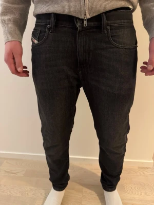 Svarta slim fit jeans från Diesel - Snygga svarta slim fit jeans från Diesel med klassisk femficksmodell och diskret logga på bakfickan. Jeansen har en något smalare passform och är tillverkade i ett mjukt denimtyg som sitter skönt. Perfekta för dig som gillar en stilren och modern look. Storlek W31 L30