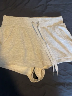 Grå mjukisshorts med snörning - Säljer ett par grå mjukisshorts med bred resår i midjan och snörning framtill. Shortsen har två sidofickor och är tillverkade i mjukt bomullsmaterial. 