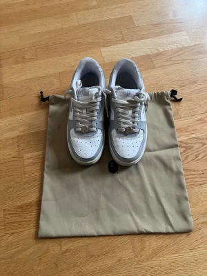 BAPE STA vita och grå sneakers - Säljer ett par BAPE STA sneakers i vitt och ljusgrått läder med den ikoniska stjärnan på sidan. Skorna har perforerad tåbox, vita snören och klassisk låg silhuett. Kommer med dustbag. Perfekta för dig som gillar streetwear och soprena detaljer.