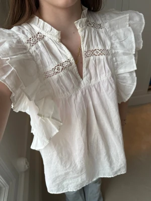 Vit volangblus från ONLY - Söt vit blus från ONLY med breda volangärmar och dekorativa spetsdetaljer framtill. Blusen har en avslappnad passform, v-ringning. Helt oanvänd.