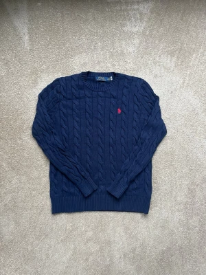 Ralph Lauren Stickad Tröja - Säljer en kabelstickad mörkblå tröja från Polo Ralph Lauren. Tröjan är varm och mysig! Inte särskilt använd och är i mycket gott skick! Hör av dig vid minsta fråga!
