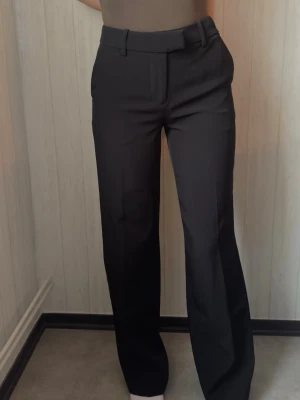 Svarta kostymbyxor från BikBok - Snygga svarta kostymbyxor från BikBok med raka ben. Byxorna har bälteshällor och stängs med dragkedja och hake. Perfekta för en clean och stilren look. Materialet känns mjukt och följsamt.