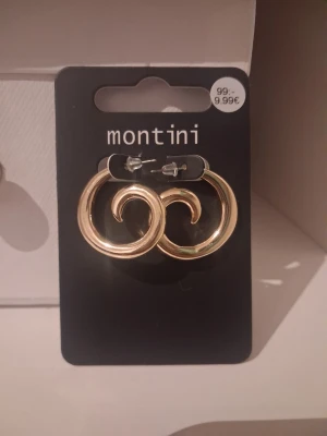 Guldiga swirl örhängen Montini nya - Säljer ett par snygga örhängen från Montini från ur&pen i guldig metall. De har en swirl-formad design som ger en cool och modern look. Perfekta för att lyfta vilken outfit som helst! Aldrig använda 