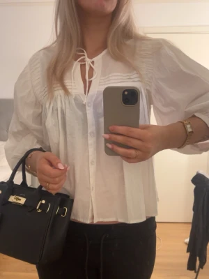 Vit luftig blus med knytband - Säljer en vit, luftig trekvartsärmad blus med knappar framtill, perfekt att styla med jeans eller kjol. Helt ny med prislapp!💕nypris-400
