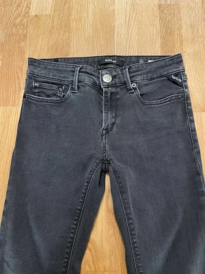 Replay Jeans - Snygga svarta jeans från Replay med klassisk femficksmodell och diskreta slitningar. Jeansen har silverfärgad knapp, svarta sömmar och Replay-logga på fickan. Materialet är stretchigt för en bekväm passform.