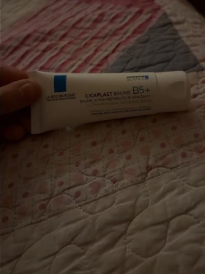 La Roche-Posay Cicaplast Baume B5+ - Cicaplast Baume B5+ från La Roche-Posay är en vit, mjukgörande och lugnande balm i tub. Perfekt för känslig eller irriterad hud. Innehåller vitamin B5 och passar både kropp och ansikte. Tuben är vit med blå detaljer och text.