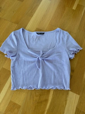 Ljuslila ribbad croppad topp - Superfin ljuslila croppad topp från Shein med ribbat tyg och knyt framtill. Toppen har korta ärmar med volangkant och en söt, feminin look. Perfekt att styla med jeans eller kjol för en trendig outfit.