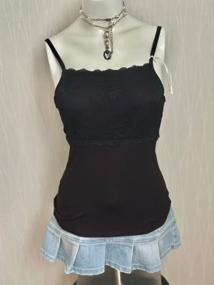Svart spetslinnetopp med smala band - Snygg svart linnetopp med smala axelband och spetsdetaljer över bysten. Toppen har en rak, figurnära passform och är perfekt för lager på lager eller sommaroutfits. Tillverkad i mjukt material med stretch för extra komfort.