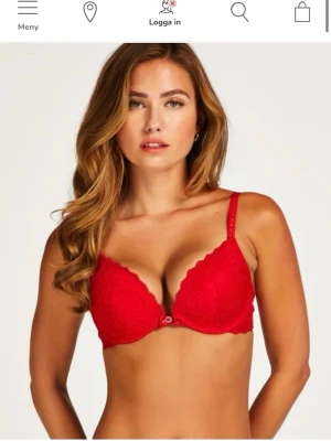 Röd spets-bh med push-up - Snygg röd bh med push-up och vadderade kupor. Bh:n har spetsdetaljer över hela framsidan och justerbara axelband. Kuporna har en lätt scallop-kant och bh:n knäpps framtill med ett litet spänne.