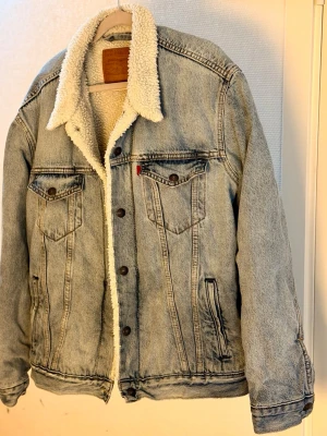 Levi's sherpa trucker jacket - Levis ikoniska denimjacka med teddyfoder. Jackan har två bröstfickor med knappar, två sidfickor och knäppning framtill. Kragen är fodrad med mjukt teddytyg. Ett måste i vår! Nypris: 1449:-, inköpt hösten 2025. Nyskick.