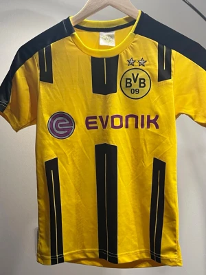 Borussia Dortmund matchtröja Reus - Säljer en gul och svart Borussia Dortmund matchtröja med Reus och nummer 11 på ryggen. Tröjan har klubbens logga, två stjärnor och sponsortryck på framsidan. Materialet är lätt och andas, perfekt för fotboll eller träning.