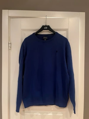 Blå tröja från Polo Ralph Lauren - Mörkblå tröja från Polo Ralph Lauren i 100% bomull. Klassisk rund halsringning och diskret broderad logga på bröstet. Perfekt basic-plagg med stilren design och långa ärmar.