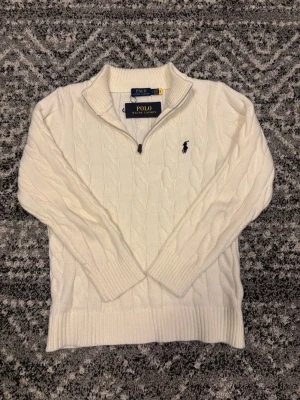 Vit kabelstickad tröja Polo Ralph Lauren - Kabelstickad vit tröja från Polo Ralph Lauren med halv dragkedja och broderad logga på bröstet. Tröjan har ribbade muddar och hög krage, perfekt för lager på lager. Klassisk och stilren design i  bomull. Tröjan är i storlek M men passar även folk i storlek S. Hör av er vid eventuell frågor eller funderingar!!