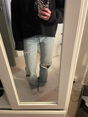 Ljusblå slitna raka jeans - Säljer ett par ljusblå jeans med raka ben och snygga slitningar vid knäna. Jeansen har klassisk femficksmodell och låg midja. Perfekta för en avslappnad och trendig look.