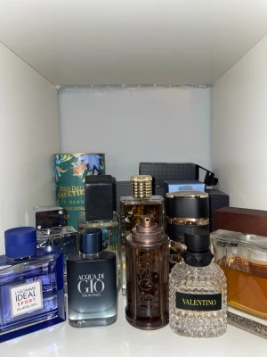 Mix av exklusiva herrparfymer - Samling med flera lyxiga herrparfymer från märken som Valentino, Hugo Boss, Armani, Guerlain, Jean Paul Gaultier och Dolce & Gabbana. Flakongerna har olika former och färger, bland annat blå, svart, guld, brons och transparent glas med detaljer i trä och metall.