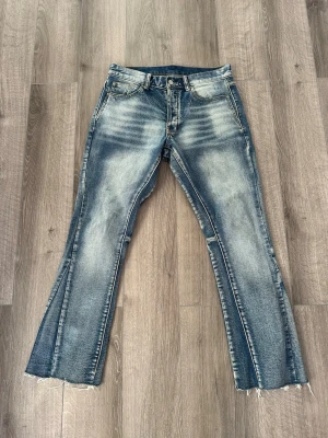 Mnml byxor  - Säljer ett par blå bootcut jeans med slitna detaljer och råa, avklippta benslut. Jeansen har klassisk femficksmodell och en snygg tvätt med ljusa partier framtill. Perfekta för en avslappnad och trendig look.