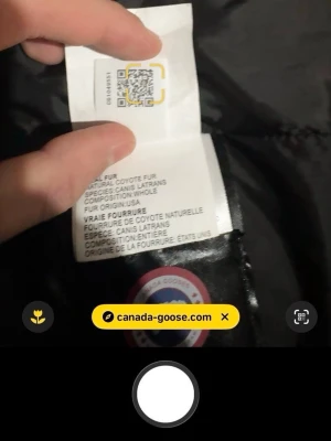 Svart dunjacka från Canada Goose - Säljer en svart dunjacka från Canada Goose med klassiskt rött och vitt märke på ärmen. Jackan har äkta coyote-pälsdetaljer och är perfekt för kalla vinterdagar. Stilsäker och varm med högkvalitativ stoppning.