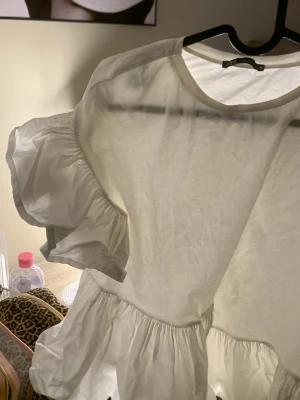 Vit volangblus från Zara🤍 - Säljer en vit blus från Zara med volangdetaljer och puffiga korta ärmar. Blusen har rund halsringning och är tillverkad i ett lätt bomullsliknande material. Perfekt för dig som gillar en romantisk och trendig stil.🫰