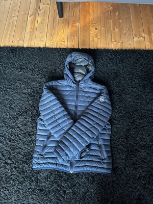 Mörkblå dunjacka med huva - Snygg mörkblå dunjacka med huva och dragkedja framtill. Jackan har två sidofickor med dragkedja och ett märke på vänster ärm. Quiltad design med horisontella sömmar som ger en modern look. Perfekt för kalla vinterdagar. Kan gå ner i pris vid snabb affär 