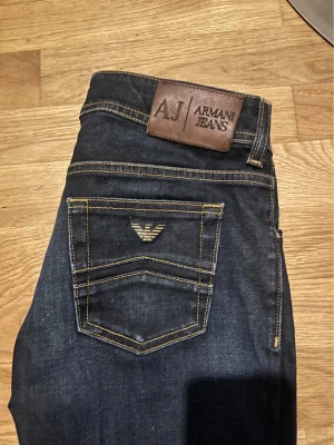 Mörkblå jeans från Armani Jeans - Snygga mörkblå jeans från Armani Jeans med klassisk femficksmodell och gul kontrastsöm. Bakfickan har den ikoniska Armani-loggan i metall och ett läderpatch med AJ-märke i midjan. Tillverkade i slitstark denim, perfekta för en trendig och stilren look. Passar folk som är ca 170. Skriv om du undrar något. Mvh Oliver