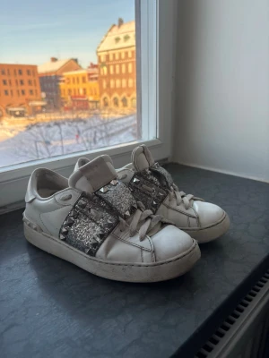 Valentino sneakers glitter & nitar – med box - .Säljer mina sneakers från Valentino. Vita skor med glitterband och nitar. Väldigt snygga och sticker ut.  ✔ Original box medföljer ✔ Bekväma sneakers ✔ Perfekta till vardag eller fest  Skorna är använda och har lite slitage, se bilder för skick.  Skicka gärna meddelande vid frågor. ✨
