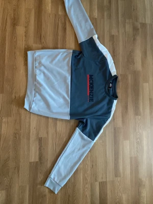 Grå och vit sweatshirt från McKenzie - Cool sweatshirt från McKenzie i grått och vitt med logga på bröstet i svart och rött. Tröjan har rund hals och långa ärmar med kontrastpaneler. Perfekt för en avslappnad streetstyle-look.