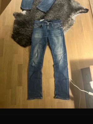 Blå raka jeans med slitningar - Säljer ett par klassiska blå jeans med raka ben och snygga slitningar framtill. Jeansen har fem fickor, normal midja och detaljerade sömmar. Tillverkade i denim med en cool tvättad look. Perfekta för en avslappnad och trendig stil.