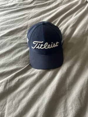  Titleist keps - Snygg mörkblå keps  från Titleist med Klassisk böjd skärm och justerbar rem bak. Perfekt för golfbanan eller som stilren accessoar!