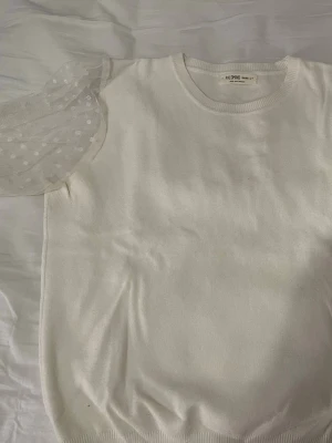 Vit topp med puffärm från Palomino - Supersöt vit topp från Palomino med transparent puffärm i mesh och prickigt mönster. Kroppen är i mjuk bomull och ärmen har en bred mudd. Perfekt för dig som vill ha något unikt och trendigt i garderoben.