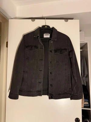 Svart jeansjacka från  - Snygg svart jeansjacka med klassisk rak passform. Jackan har två bröstfickor med lock, knäppning framtill och markerade sömmar. Tillverkad i kraftigt denimtyg som ger en cool och avslappnad look.