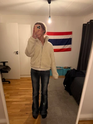 Beige fluffig stickad zip-tröja - Mysig och fluffig stickad jacka i beige med dragkedja framtill och hög krage. Perfekt för att hålla sig varm under kyliga dagar. Jackan har långa ärmar och en avslappnad passform. Materialet är mjukt och känns skönt mot huden.