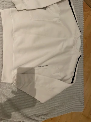 Vit sweatshirt från Calvin Klein Jeans - Säljer en stilren vit sweatshirt från Calvin Klein Jeans med svarta detaljer längs ena sidan och diskret logga på framsidan. Tröjan har rund halsringning och är tillverkad i mjukt bomullsmaterial. Perfekt för en clean och modern look.