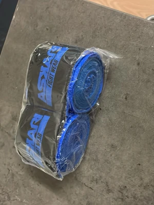 Blå boxningslindor från Askari 4,5 m - Säljer ett par blå boxningslindor från Askari Fight Wear. Lindorna är tillverkade i elastiskt material och har svart logotyp med blå text. Perfekta för att skydda händer och handleder under träning eller match.