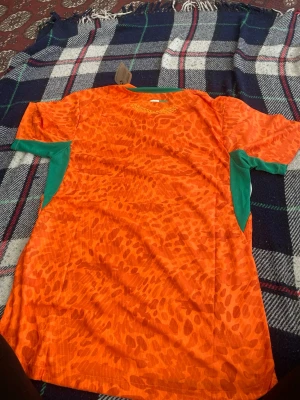 Orange leopardmönstrad t-shirt - Cool orange t-shirt med leopardmönster och gröna detaljer på sidorna. Perfekt för dig som vill sticka ut med färg och mönster. Skön passform och korta ärmar, passar till många olika stilar.