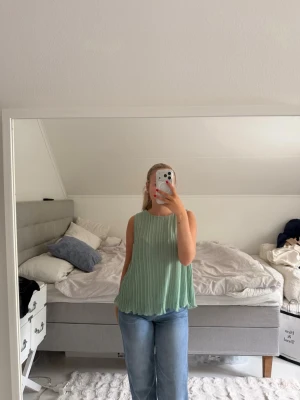 Plisserad mintgrön ärmlös topp - Säljer en flowy, plisserad mintgrön topp med rund halsringning. Toppen är ärmlös och har en lös passform som ger ett luftigt intryck. Perfekt för varma dagar och enkel att styla med jeans eller kjol.
