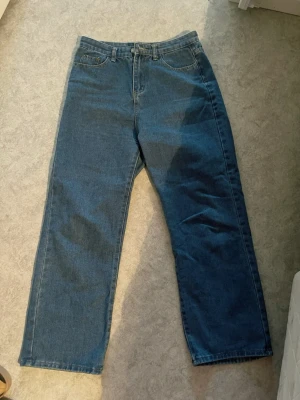 Blå raka jeans med hög midja - Säljer ett par klassiska blå jeans med rak passform och hög midja. Jeansen har fem fickor, bälteshällor och stängs med dragkedja och knapp. Tillverkade i kraftigt denimtyg som ger en tidlös look. Okänt märke, men jag tror den är från Shopee, ca ~199-299kr. Säljer för 150kr. Sparsamt använd, utan defekter. Sista bilderna är en REFERENS inte riktiga byxorna då jag inte hittar dom online