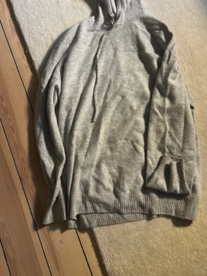 Ljusgrå hoodie marinull  - En enkel och stilren ljusgrå hoodie med huva och dragsnören. Hoodien har ribbade muddar vid ärmslut och nederkant. Perfekt för en avslappnad look och passar till det mesta. Materialet känns mjukt och bekvämt.