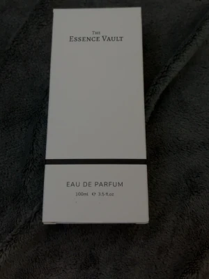 The Essence Vault 950 Eau de Parfum - The Essence Vault 950 Eau de Parfum i en stilren, rektangulär glasflaska med silverfärgad spraykork. Flaskan rymmer 100 ml och har en enkel vit etikett med svart ram. Förpackningen är vit med minimalistisk design. Inspired by Layton