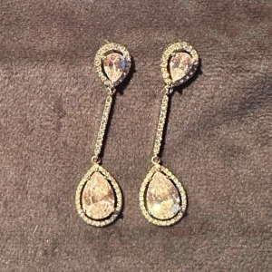 Eleganta Droppformade Bling Örhängen - Örhängena har en modern design med två droppar kopplade med en rad små klara stenar. Använda ett fåtal gånger, men i jättefint skick.