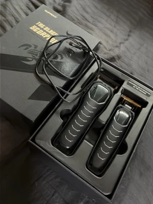 Svarta hårtrimmers med guldfärgade blad - Två svarta hårtrimmers med guldfärgade blad, perfekta för styling och trimning av hår eller skägg. Ergonomisk form med räfflad yta för bättre grepp. Passar både till detaljtrimning och större ytor. Tillverkade i plast och metall.