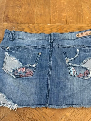 Blå jeanskjol med broderade detaljer - Säljer en blå jeanskjol från med slitna kanter och broderade detaljer på bakfickorna. Så fin men har för många jeanskjolar. Alla mått finns med på bilderna! Perfekt nu på sommaren och till skolstart.