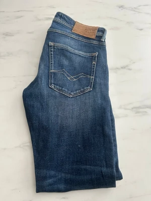 Blå jeans från Replay - Snygga blå jeans från Replay med klassisk femficksmodell och ljus kontrastsöm. Bakfickan har ett unikt broderat mönster och ett litet 'R'-märke. Jeansen har en skinnpatch med Replay-logga i midjan. Perfekta till en avslappnad stil.