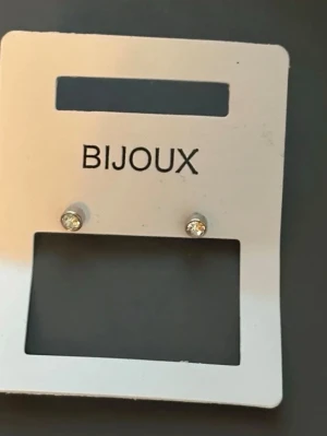 Silvriga örhängen med klar sten Bijoux - Säljer ett par stilrena silvriga örhängen från Bijoux med små, klara stenar framtill. Örhängena är diskreta och runda, perfekta för dig som gillar minimalistisk stil. Materialet ser ut att vara metall med glittrande steninfattning.