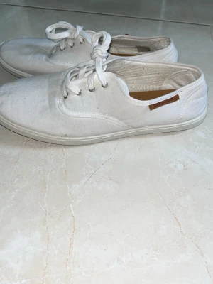 Vita seglarskor från Marstrand - Säljer ett par klassiska vita seglarskor från Marstrand. Skorna är i canvas med vita snören och har en liten brun detalj på sidan. Insidan är fodrad i ljust material och sulan är vit. Perfekta för en clean och avslappnad stil.