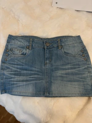 jeanskjo - Trendig ljusblå jeanskjol i kort modell med dekorativa knappar och fem fickor. Köpt här på Vinted men var för liten. Skulle säga stolek S-XS
