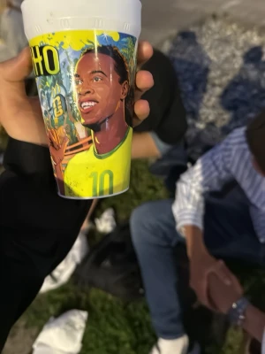 Plastmugg med fotbollsmotiv - Säljer en färgglad plastmugg med tecknat fotbollsmotiv och texten '10' samt 'ALDINHO'. Muggen har illustrationer av en fotbollsspelare i gul tröja, gröna detaljer och en fotboll. Perfekt för dig som gillar sportiga accessoarer.