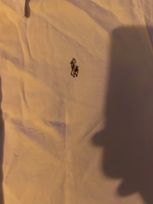 Vit skjorta från Ralph Lauren - Klassisk vit skjorta från Ralph Lauren med broderad logga på bröstet. Skjortan har knappar framtill, lång ärm och en tidlös krage. Perfekt för dig som gillar stilrena och ikoniska plagg.
