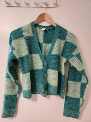Lindex Grönrutig stickad kofta storlek 146 - Lindex Snygg stickad kofta i gröna och ljusgröna rutor. Koftan har v-ringning, tre stora gröna knappar framtill och långa ärmar. Perfekt för dig som gillar retrovibbar och vill ha något mysigt och trendigt i garderoben.